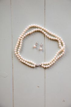 A pearl neckalce and some earrings are waiting on the table for the bride to finish getting ready and put on her jewelry.