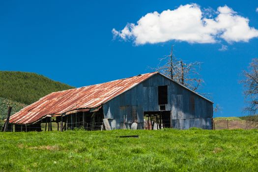 Rusty old farm barn structure in farming pastures during the summer.