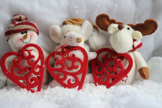 Three happy christmas toys with red hearts in the snow