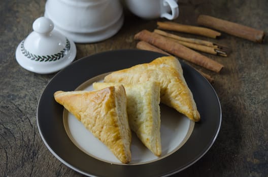 Puff pastry on the plate with cinnamon sticks  over wooden background