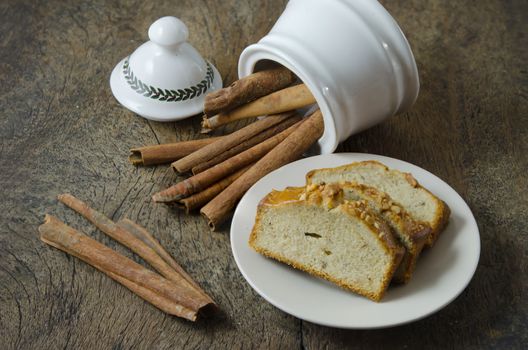 White  bowl with cinnamon sticks and slice of banana cake on plate
