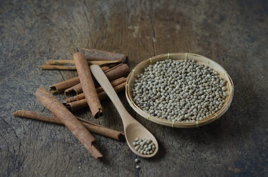 cinnamon sticks and peppercorns on basket with spoon over wooden background