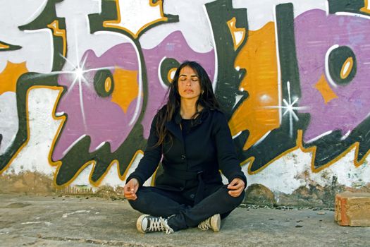 Young woman meditating at a graffiti brick wall