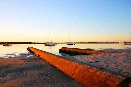 Still and serene sunrise over beach with water overflows and boats.
