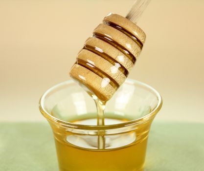 Honey dipper dunked into a glass of honey and lifted.