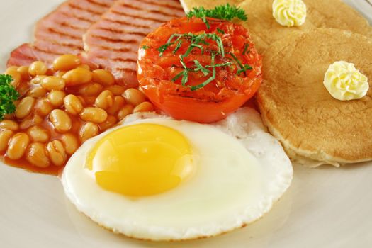 Breakfast of grilled bacon, tomato, egg, baked beans and pancakes.