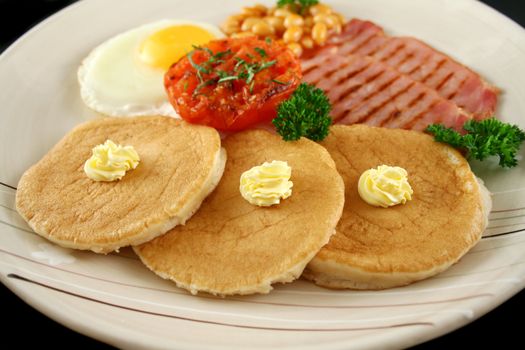 Breakfast of grilled bacon, tomato, egg, baked beans and pancakes.