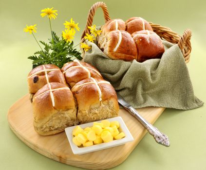 Hot cross buns in a basket and some with butter and daisies.