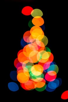 Blurred colorful lights as a silhouette of Christmas tree on black