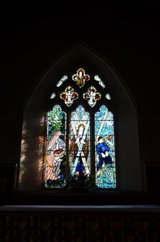 Brightly coloured stained glass window above a church alter In England.
