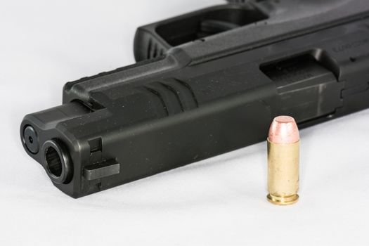 Tip of black hand gun and a bullet on white background