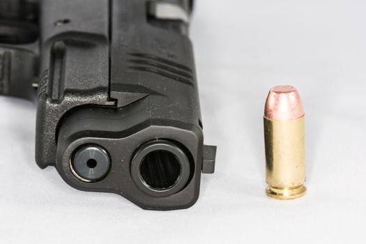 Tip of black hand gun and a bullet on white background