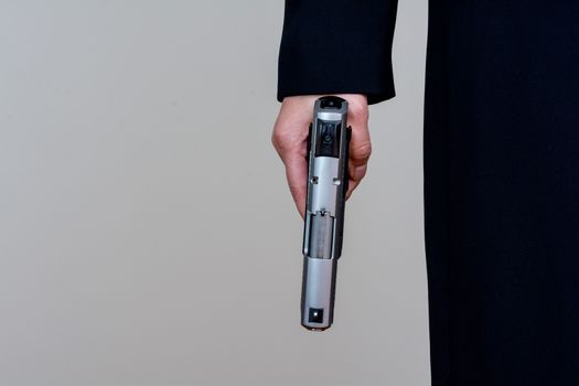 Woman in business suit holding a hand gun by her side on gray background