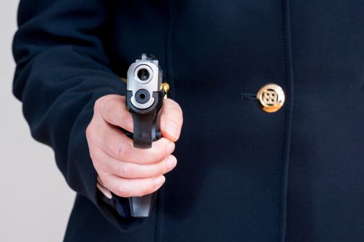 Close up of woman in business suit pointing a hand gun at you  on gray background
