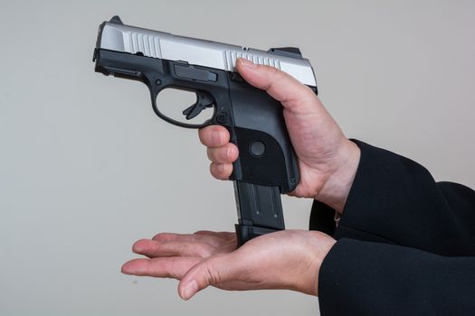 Close up of woman in business suit loading a pistol on gray background