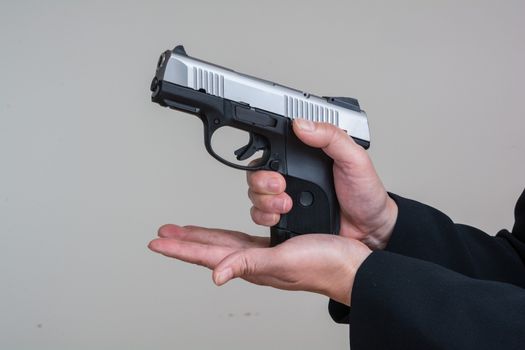 Close up of woman in business suit loading a pistol on gray background