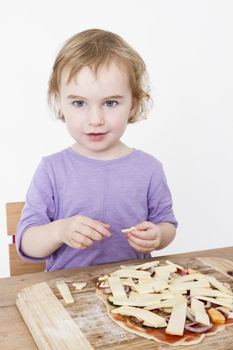young child putting cheese on homemade pizza. studio shot with light grey background