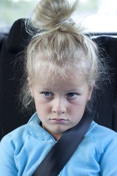 A sulky child in the back of the car with seatbelt on