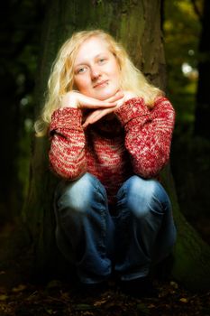 Atmospheric portrait of a charismatic young blond woman sitting outdoors in the darkness with her chin resting on her hands smiling at the camera