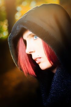 Head and shoulders portrait of a beautiful redhead woman with blue eyes standing in profile outdoors wearing a hooded anorak