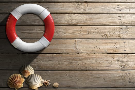 Red and white lifebuoy hanging to a wooden wall with seashells and sand
