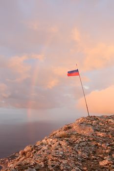 Russian flag on the top of a mountain on the background of the sea with a rainbow. Crimea, Ukraine