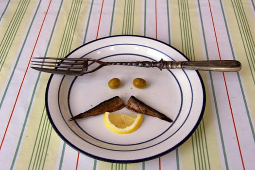 fork with knife on dish with olive, fish  and lemon