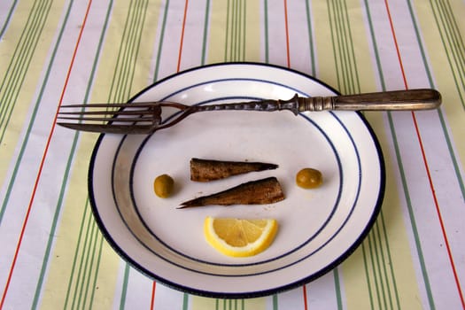 fork with knife on dish with olive, fish  and lemon