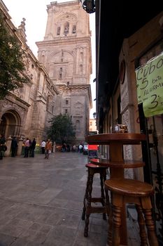 Belltower of the Cathedral and table and bar stools on Carcel Baja street, Granada, Spain