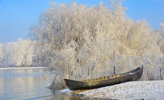 Frosty winter trees and boat near Danube river