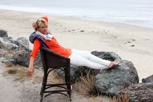 Side view of adult woman looking away while sitting on a wooden chair at grassy beach Half moon bay. California
