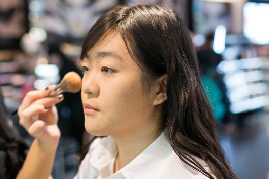 Young Asian woman applying facial powder with a brush