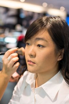 Young Asian woman applying facial powder with a brush