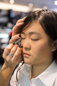 Young Asian woman applying eye liner with a small brush