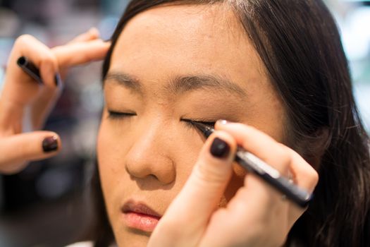 Young Asian woman applying eye liner with a small brush