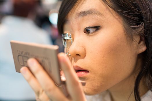 Young Asian woman fixing her eye lash with clipper