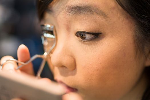 Young Asian woman fixing her eye lash with clipper