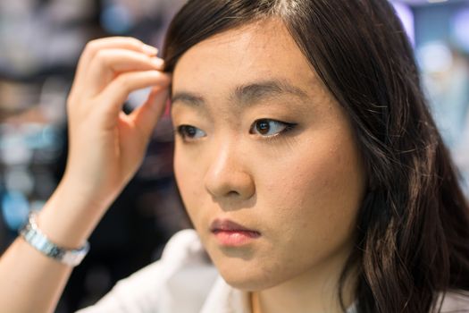 Young Asian womna checking herself while applying cosmetics
