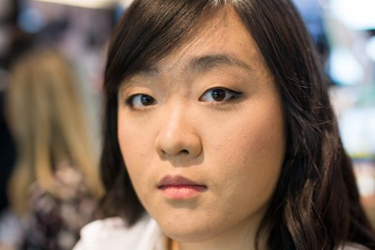 Young Asian womna checking herself while applying cosmetics