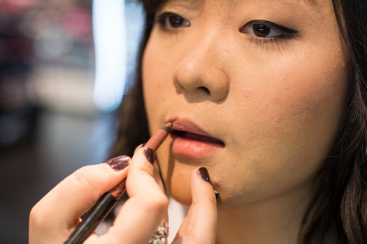 Young Asian woman applying lipstick and other cosmetics