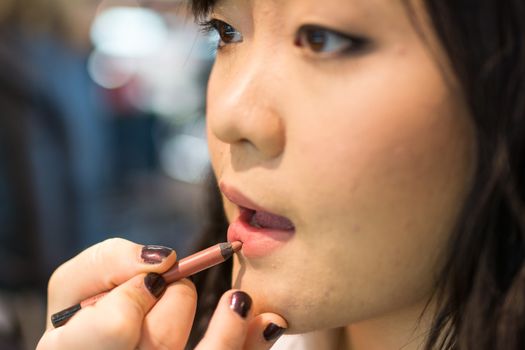 Young Asian woman applying lipstick and other cosmetics