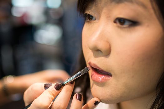 Young Asian woman applying lipstick and other cosmetics