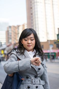 Young Asian woman checking her watch on a street in a large city