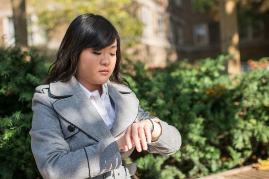 Young Asian woman checking her watch on a street in a large city