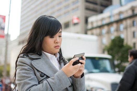 Young Asian woman texting and walking on a street in a large city