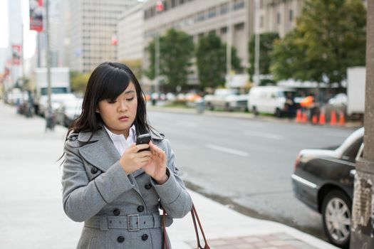 Young Asian woman texting and walking on a street in a large city