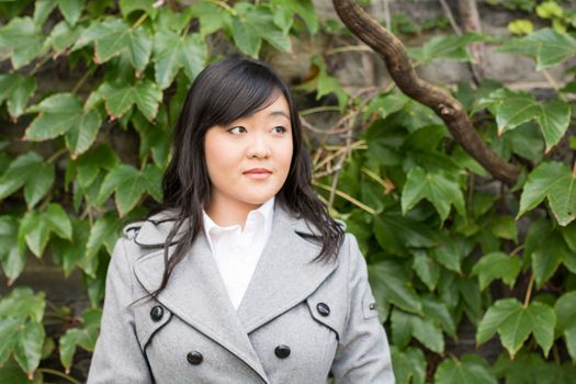 Young Asian woman standing next to leafs on a wall and smiling