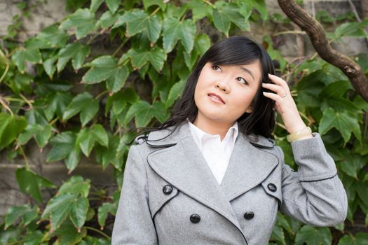 Young Asian woman standing next to leafs on a wall and smiling