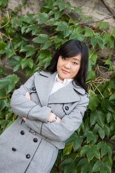 Young Asian woman standing next to leafs on a wall crossing arms