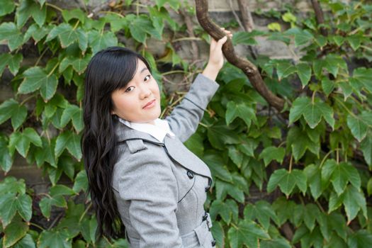 Young Asian woman standing next to leafs on a wall holding a branch